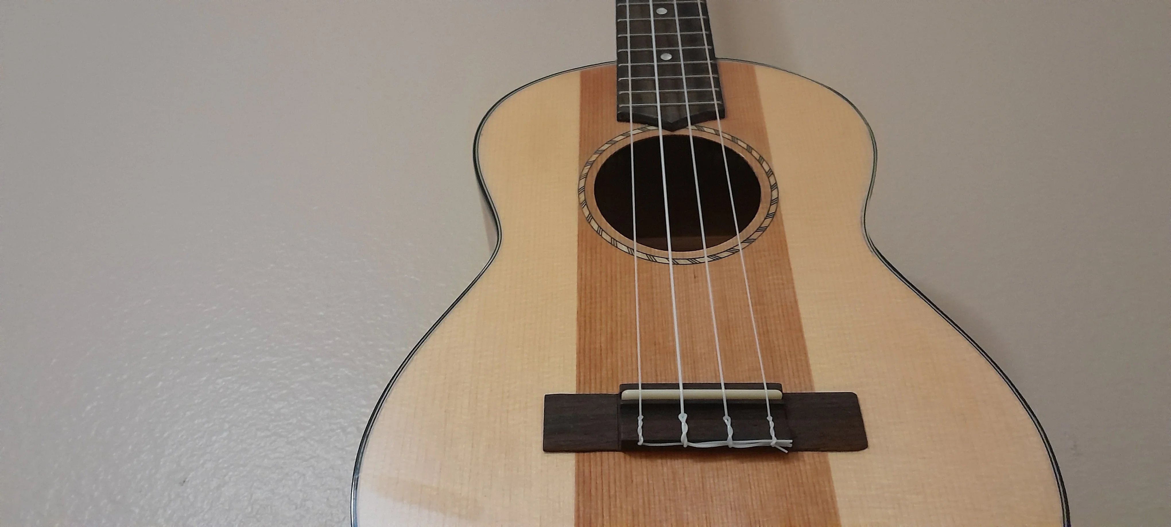 Ukulele close-up showing bridge, strings, and spruce top